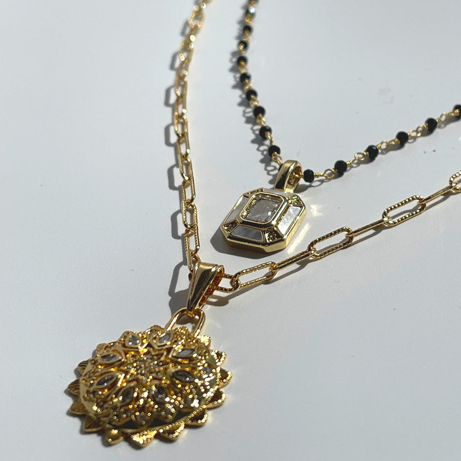 Gold necklace with intricate pendant on a light gray background